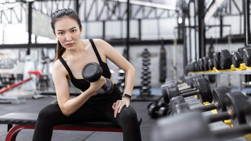 lady paying attention on carrying a dumbbell with her right hand while sitting on the bench