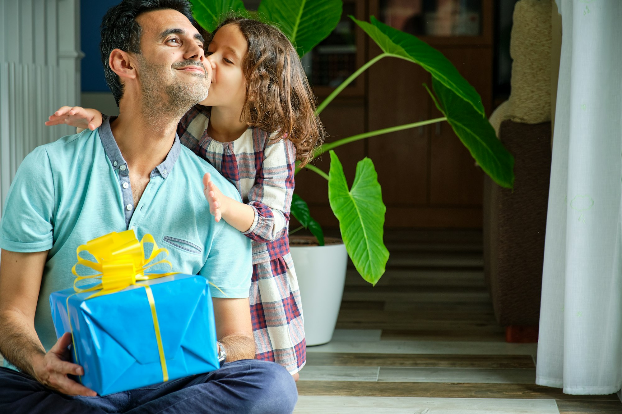 little girl who just gave a gift to her father giving him a kiss