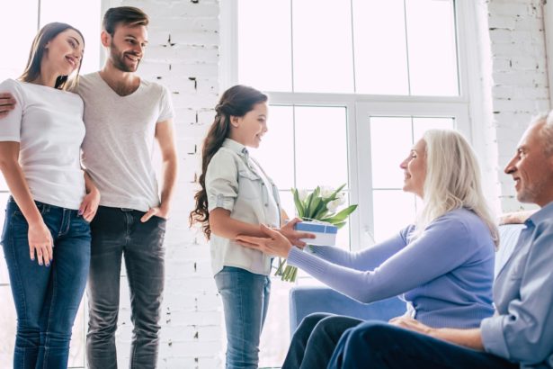 The girl with parents giving a gift with flowers to grandparents.