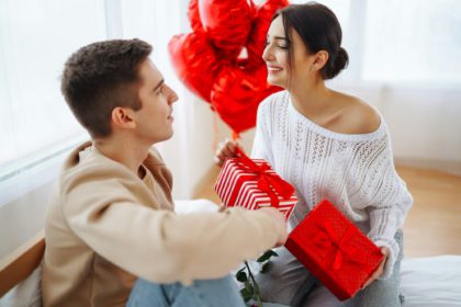 Young couple at home celebrating Valentine's Day. Exchange of gifts. Surprise and love concept.
